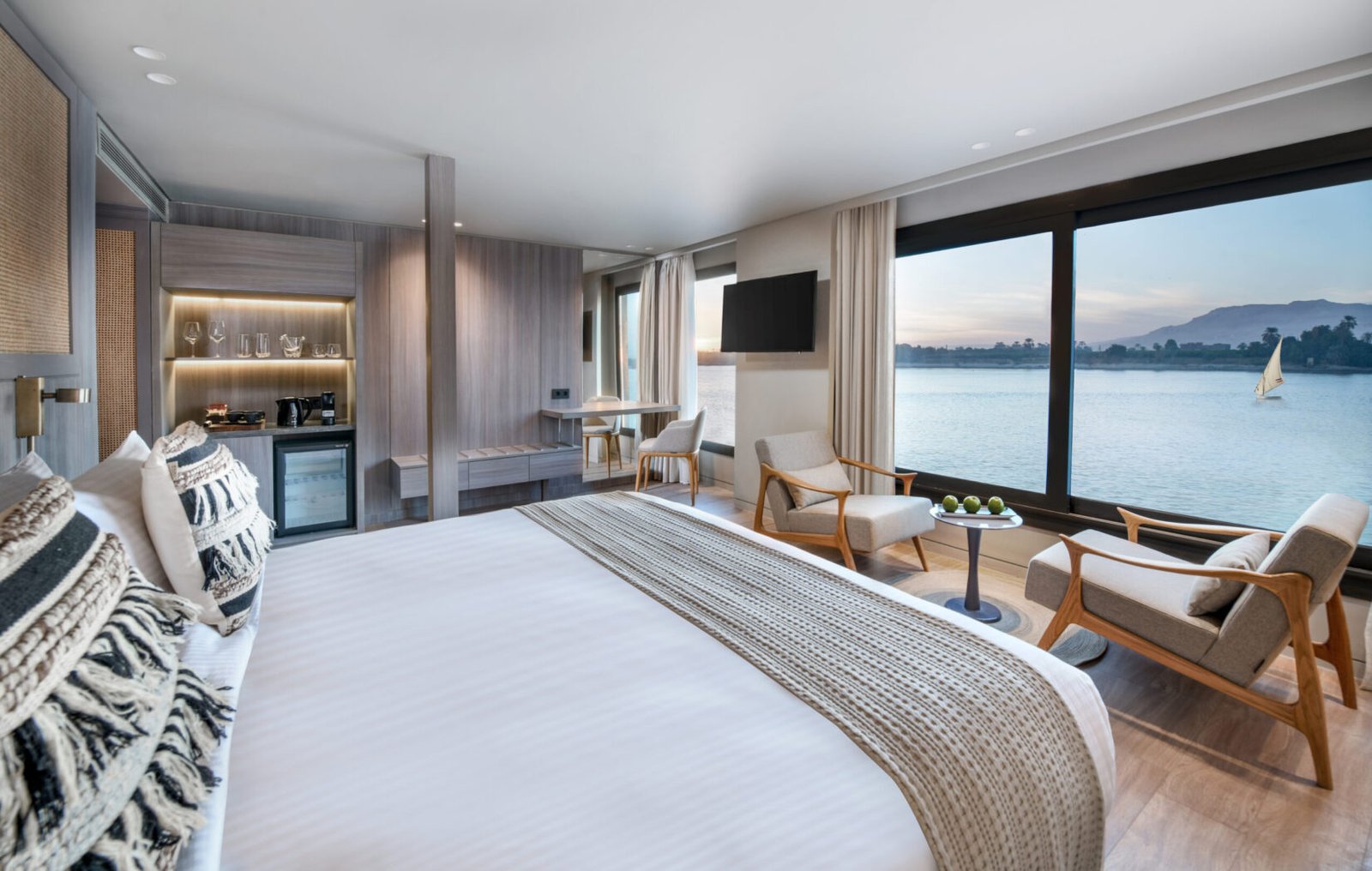 The luxurious and elegantly designed cabin on the Historia Nile Cruise, featuring a plush king-size bed and a large window with a scenic view of the Nile