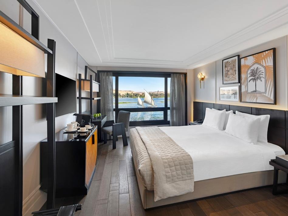 A bright and modern standard cabin on the Movenpick Sunray Nile cruise, featuring a comfortable bed and a large panoramic window with a direct view of the Nile