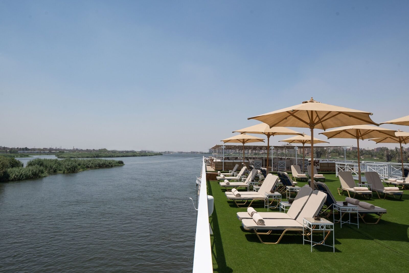 Sunny sundeck and swimming pool aboard the Jaz Regent Nile Cruise, with lounge chairs and a clear view of the Nile River and green riverbanks