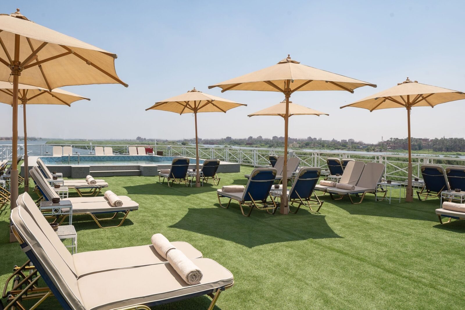 Wide shot of the M/S Jaz Regent's top deck, showing the blue swimming pool, sun loungers, and an expansive panoramic view of the Nile River