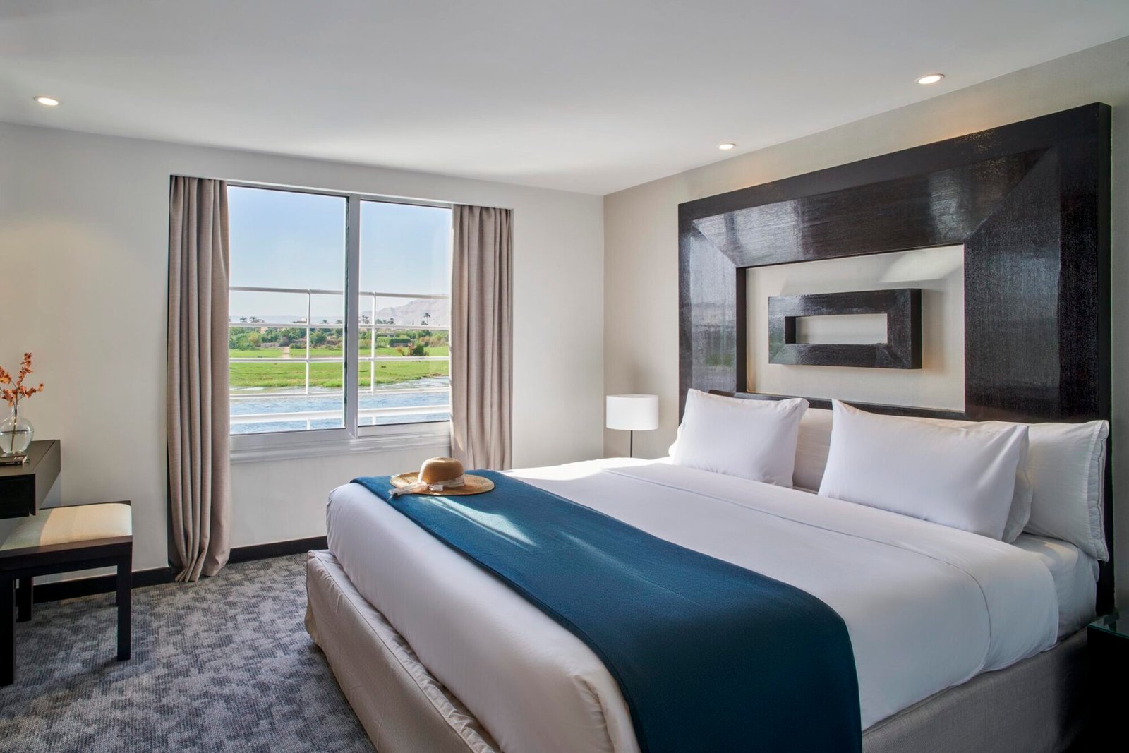 A beautifully appointed luxury cabin on the Movenpick Royal Lily Nile cruise, with a large bed, elegant furniture, and a window view of the Nile River.