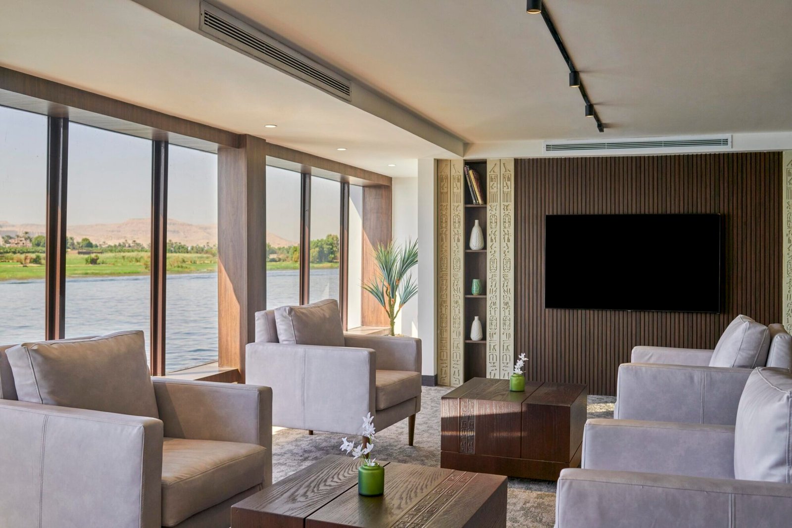 A luxurious and comfortable lounge area inside a Movenpick Nile cruise ship, with plush sofas and large windows offering a scenic view of the Nile River.