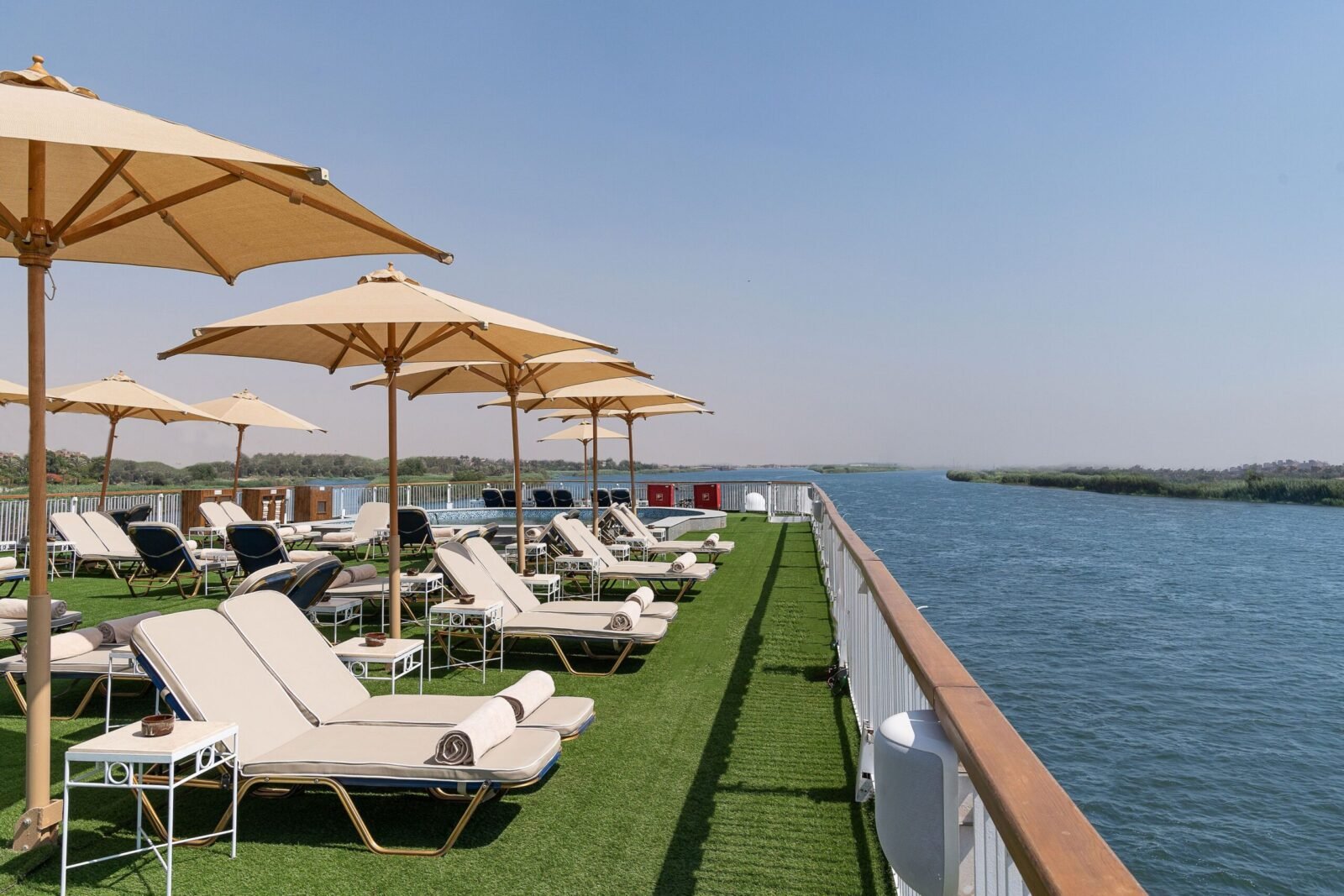 Photo of the spacious sundeck and swimming pool aboard the Jaz Viceroy Nile Cruise ship, with the view extending to the green banks of the Nile River.