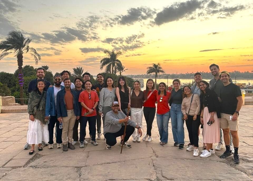Nile Cruisen team smiling on a 5-star luxury cruise ship deck with the Nile River in the background.