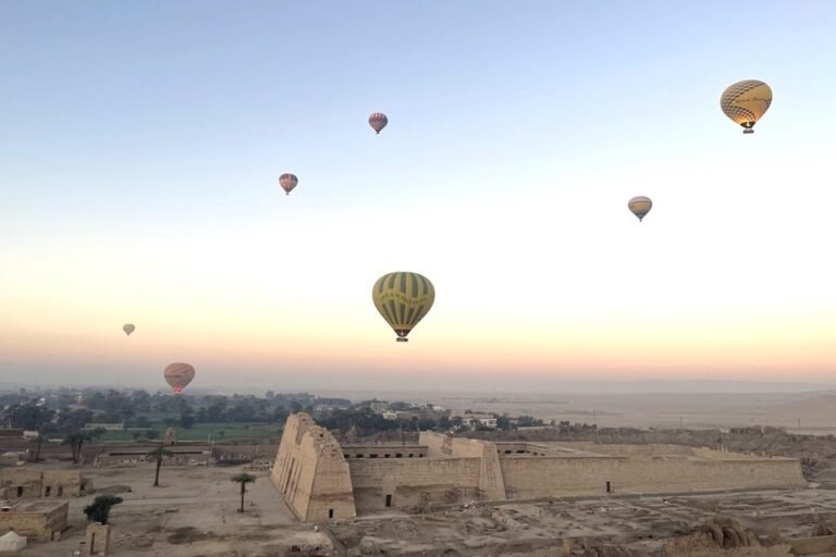 A fleet of colorful hot air balloons peacefully floating over the Valley of the Kings and ancient temples in Luxor, Egypt, during a golden sunrise.