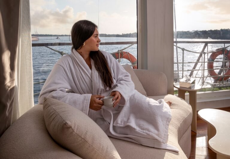 A stunning view of the Nile River from a cruise ship while sailing, featuring a person relaxing in a lounge chair, the cruise booked by NIle Cruisen