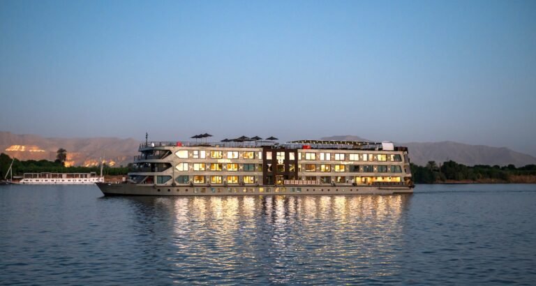 A luxury five-star Nile cruise ship with a sun deck pool sailing on the Nile River at sunset, featuring traditional Egyptian landscapes in the background.