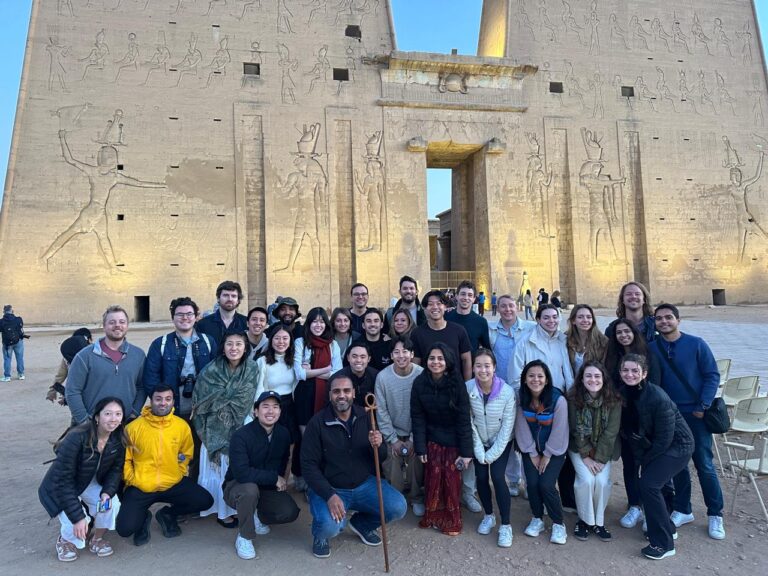 A group of tourists standing in front of the ancient stone columns and colossal statues of Luxor Temple in Egypt, listening attentively to a tour guide from Nile Cruisen.