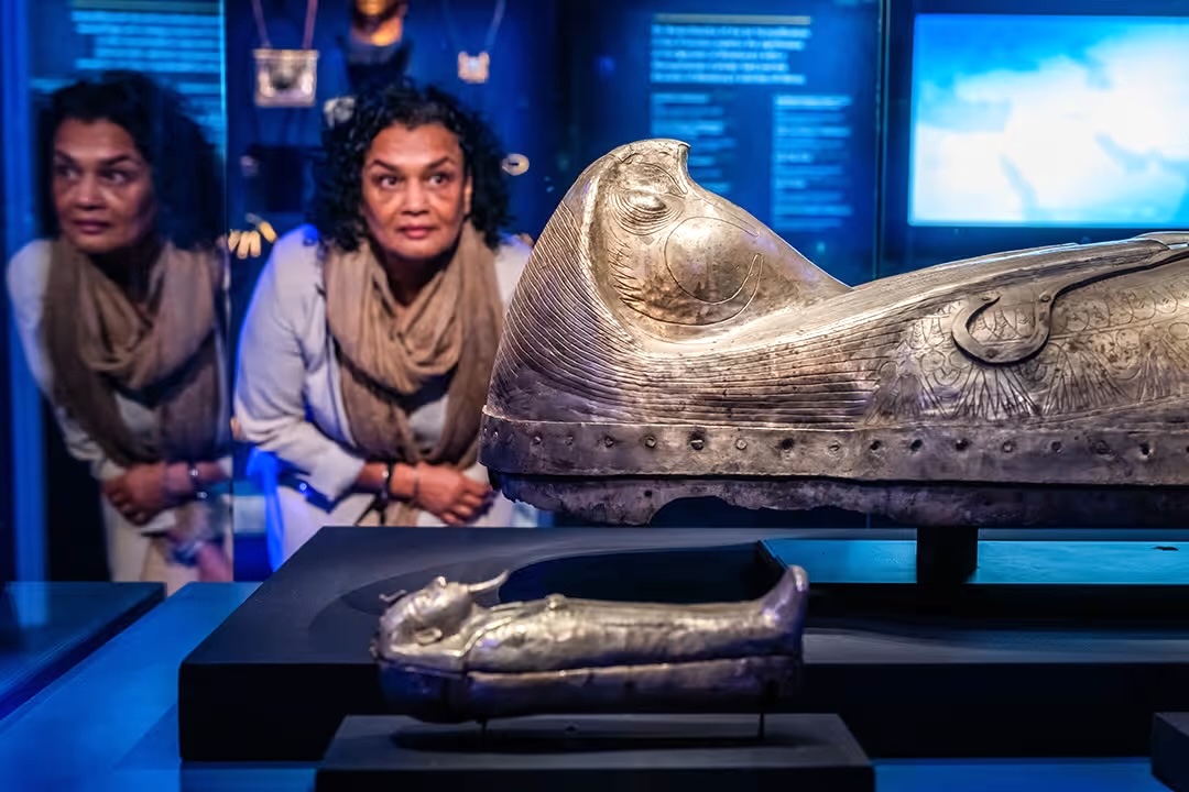 A woman admiring the falcon-headed sarcophagus of King Ramses II during an ancient Egyptian exhibition.